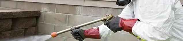 Pest control technician applying exterior insect treatment along a home foundation in Las Vegas, NV
