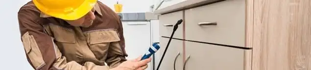 Roach exterminator applying treatment under kitchen cabinets in Las Vegas, NV