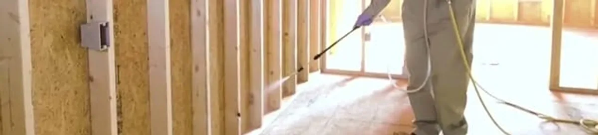Termite treatment technician applying spray along framing and unfinished walls in Las Vegas, NV