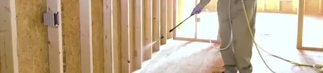 Termite treatment technician applying spray along framing and unfinished walls in Las Vegas, NV